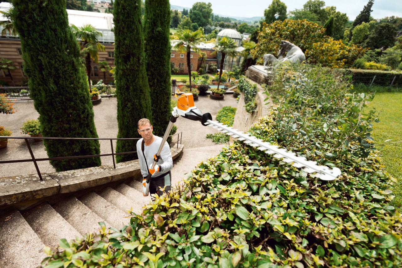Man on a staircase cuts high hedges with the STIHL HLA 85 cordless hedge cutter