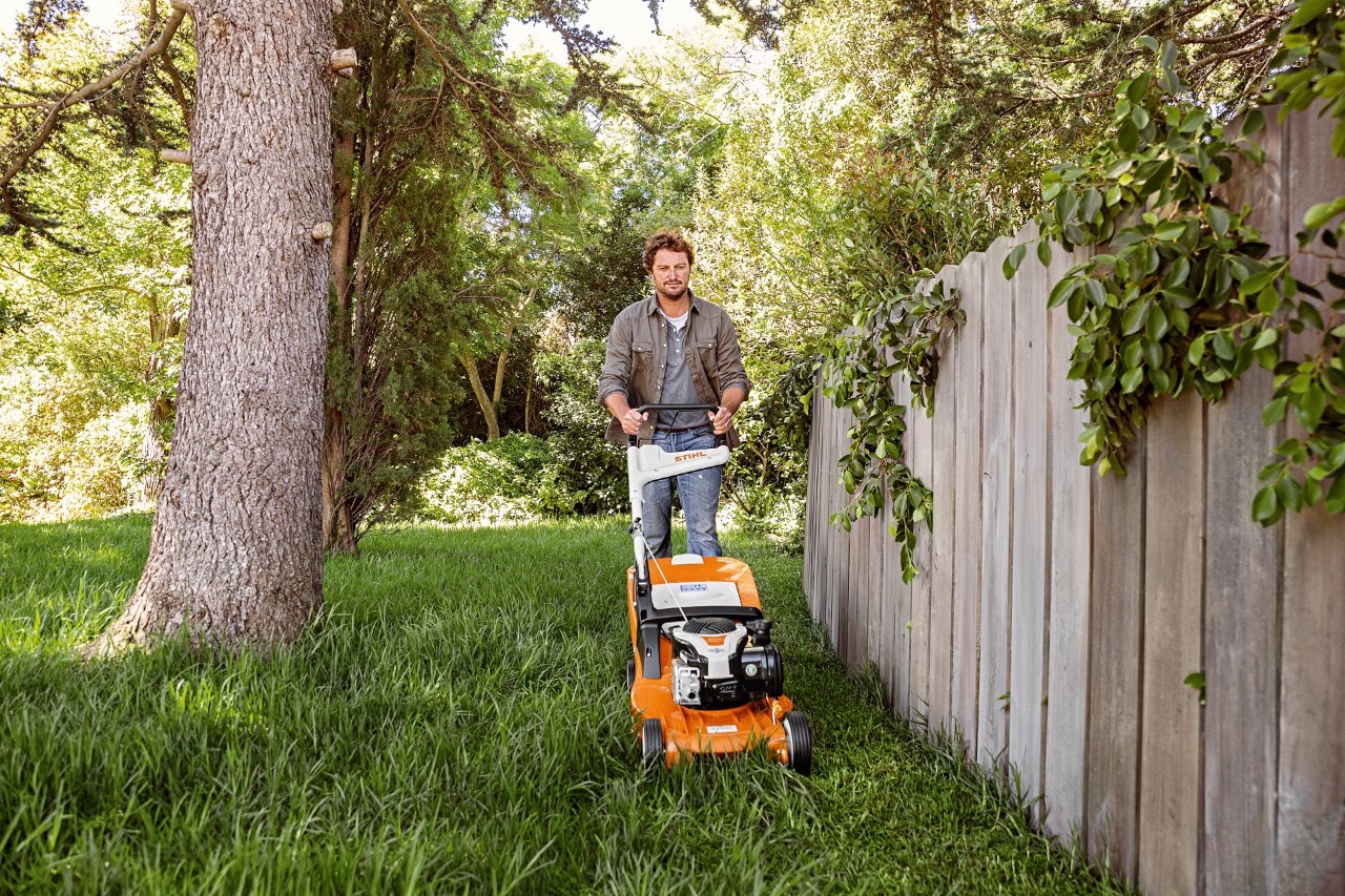 A man using a STIHL RM 448 TC petrol lawn mower on grass next to a wooden fence