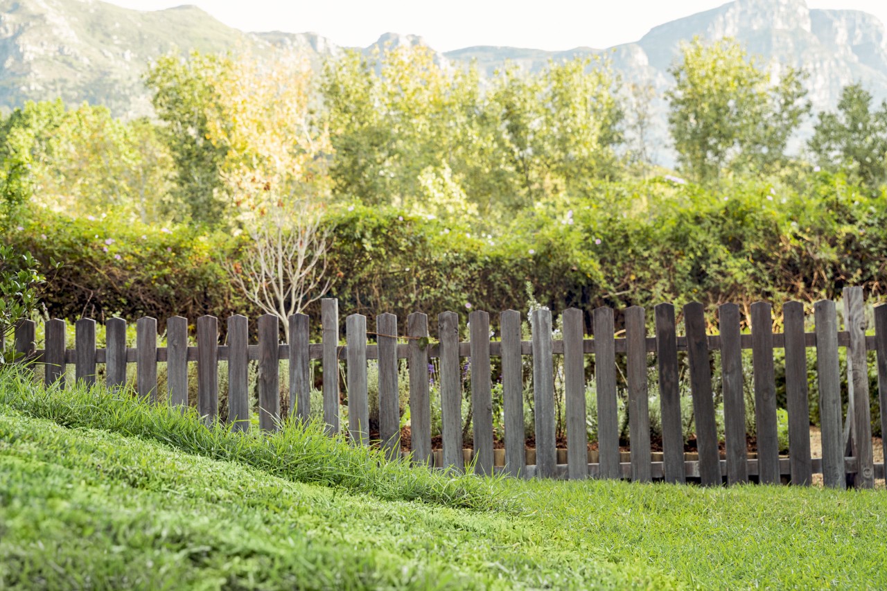 A sloping green lawn with a fence and trees and mountains visible in the distance