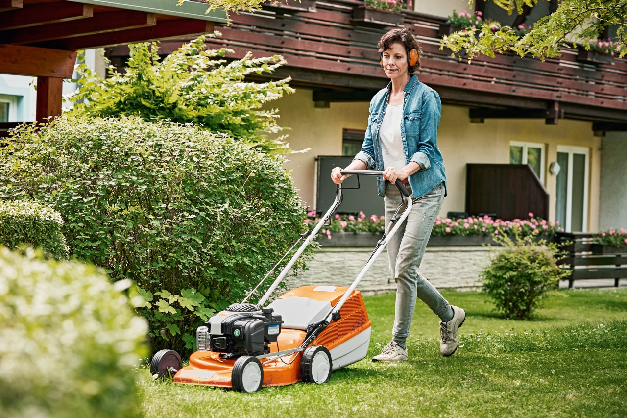 Woman treats her lawn in spring with a STIHL RM 243 T petrol lawnmower in the garden in front of a house