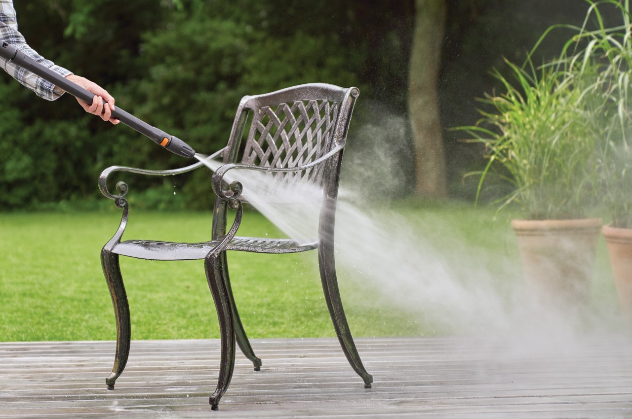 A metal garden chair being cleaned with a jet of water from STIHL RE 130 Plus high-pressure cleaner