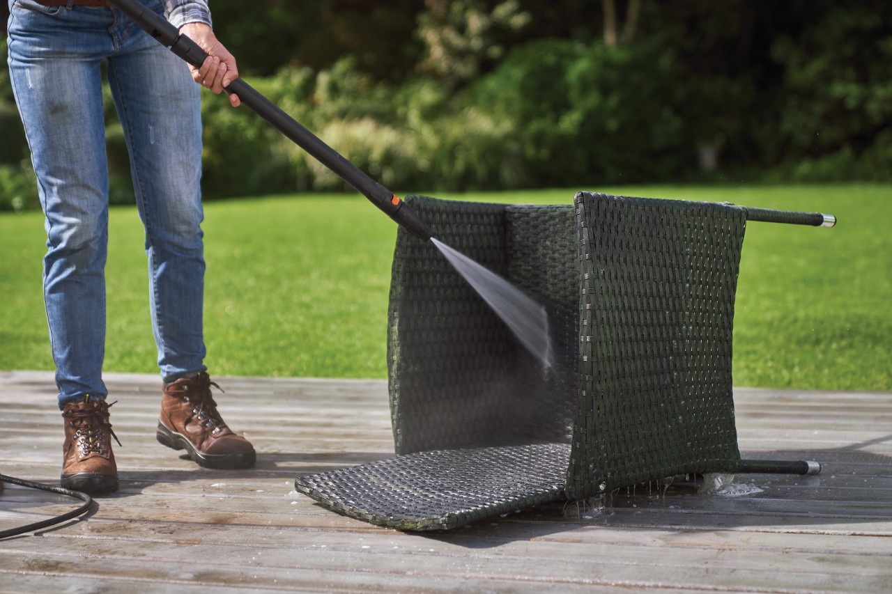 A rattan chair lying on its back, being cleaned with a STIHL RE 130 Plus high-pressure cleaner