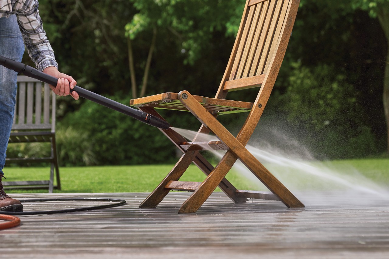 A wooden garden chair on a patio being cleaned with a jet of water from a STIHL RE 130 Plus high-pressure cleaner