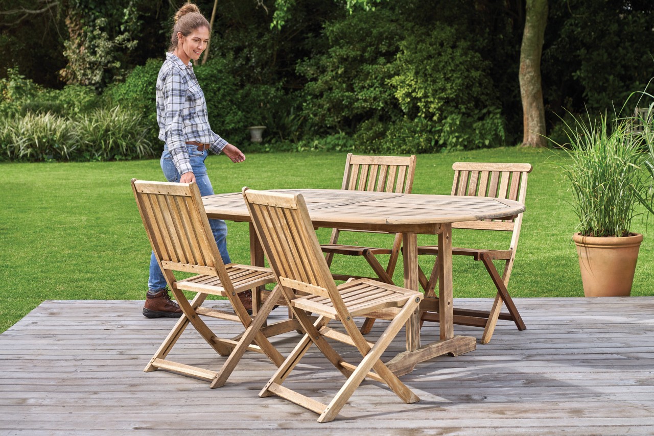 A woman inspects clean wooden garden furniture on a patio, with a STIHL RE 130 Plus high-pressure cleaner beside it