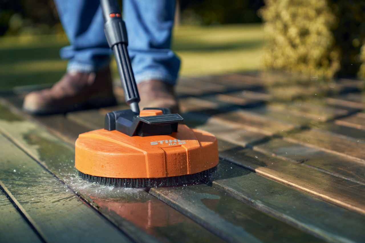 Close-up of the STIHL RA 82 surface cleaner being used to clean wooden decking, with the user’s feet behind it