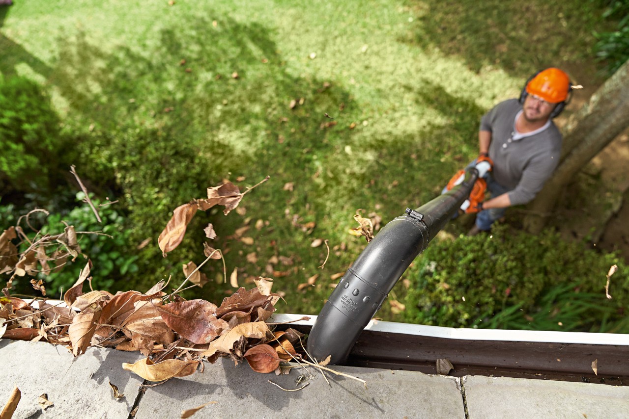 Overhead shot of a gutter full of leaves being cleaned by a man with a STIHL leaf blower and gutter cleaning set