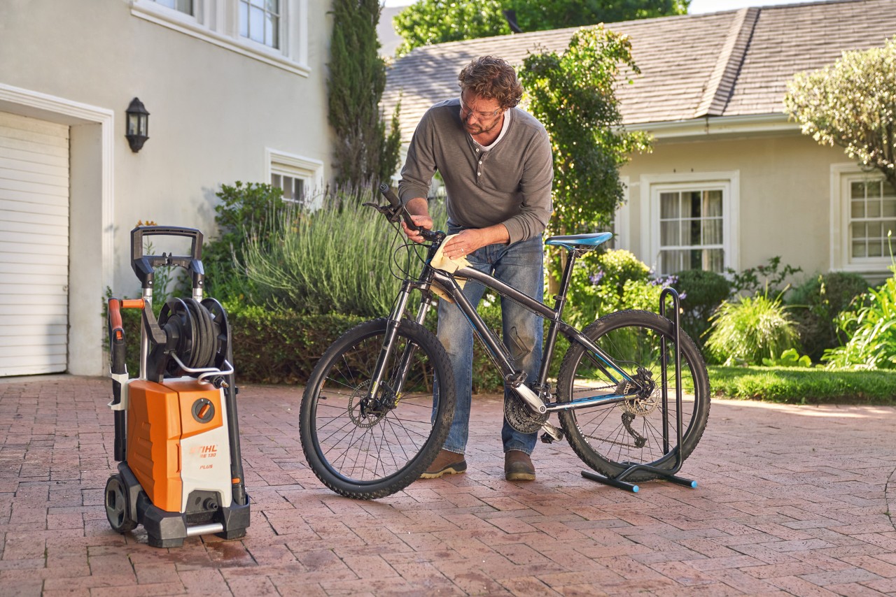 A man drying a bicycle with a cloth, with a STIHL RE 130 plus pressure washer beside him