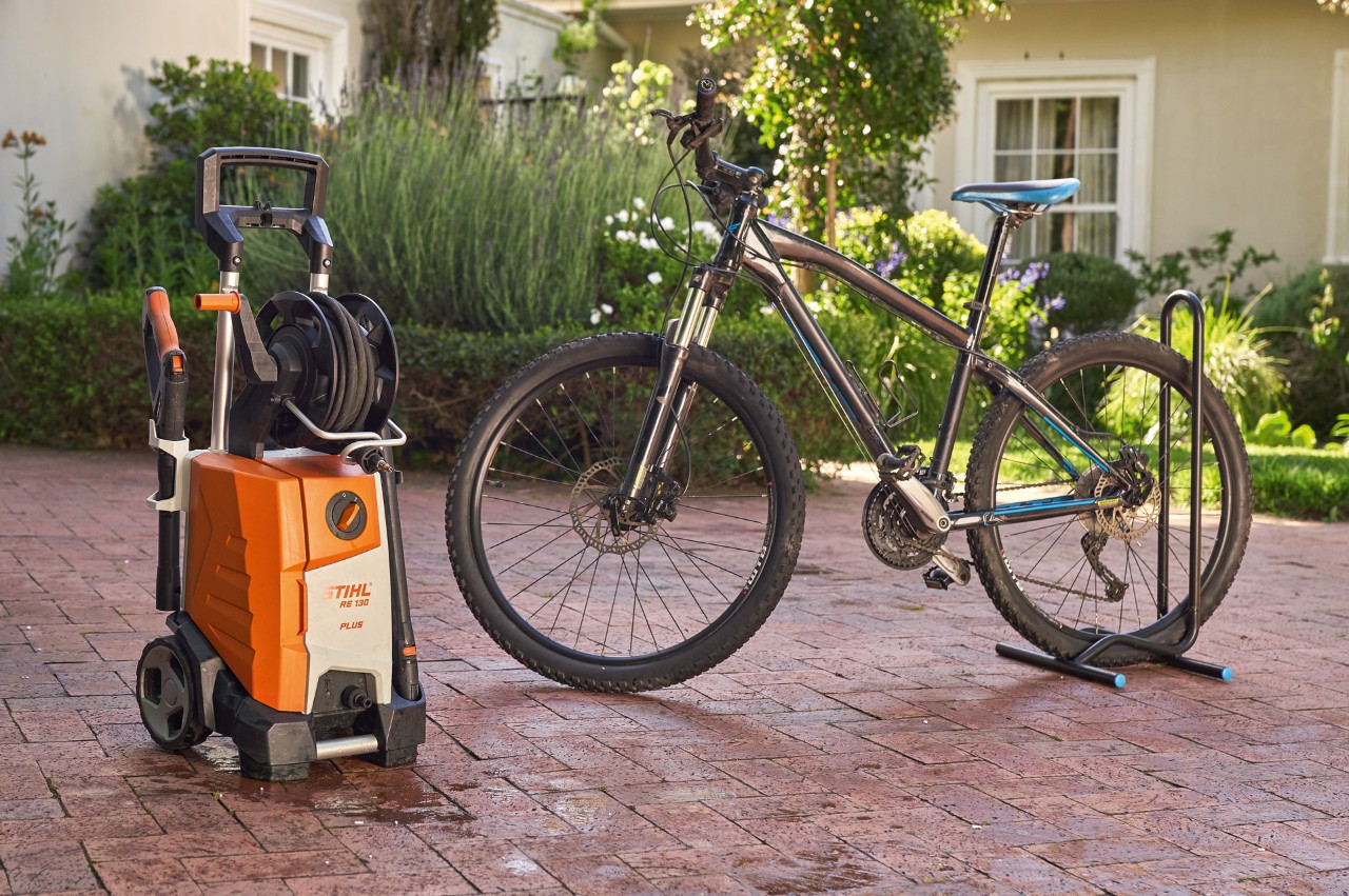 A freshly washed bike standing in front of a house next to a STIHL RE 130 plus high-pressure cleaner