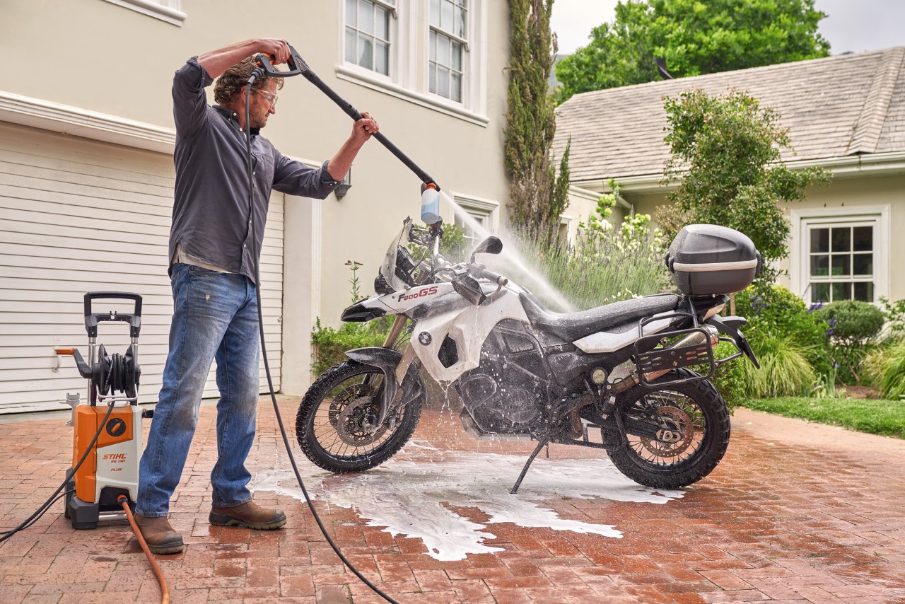 A man using the STIHL RE 130 plus pressure washer to spray vehicle shampoo onto a motorcycle 
