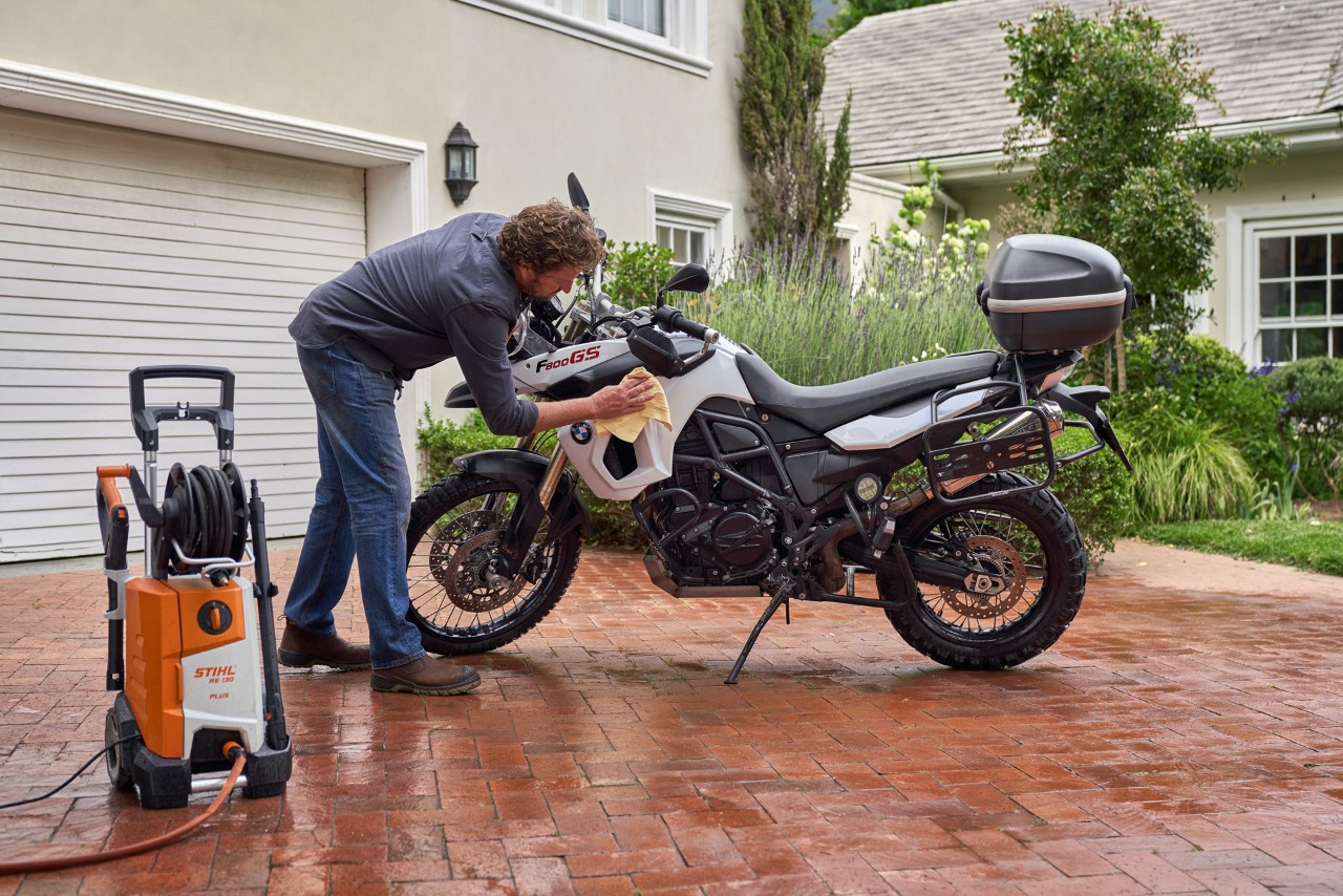 A man drying a motorcycle with a chamois cloth, with a STIHL RE 130 Plus pressure washer beside him