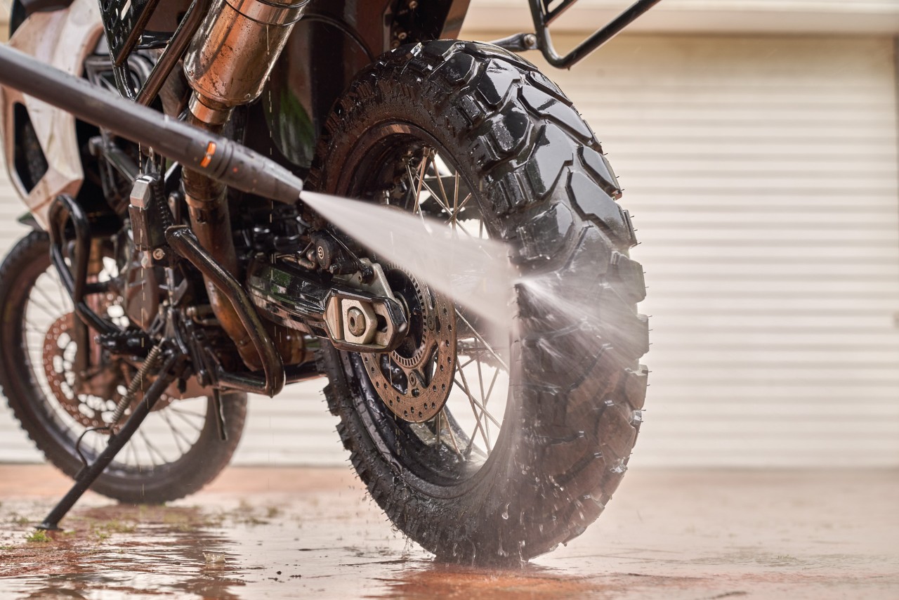 Close-up of a water jet and pressure washer hose cleaning the back wheel of a motorcycle