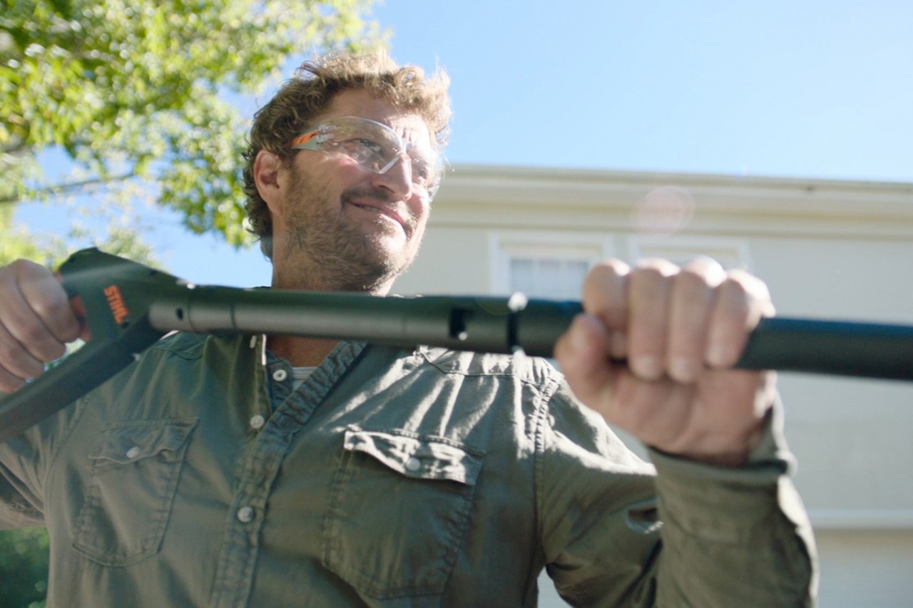 A smiling man wearing protective glasses and holding the handle of a STIHL RE 130 Plus pressure washer