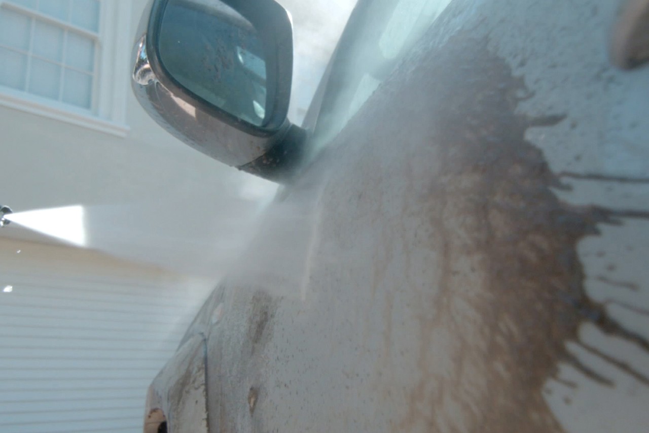 Close-up of a dirty car door being washed with a pressure washer