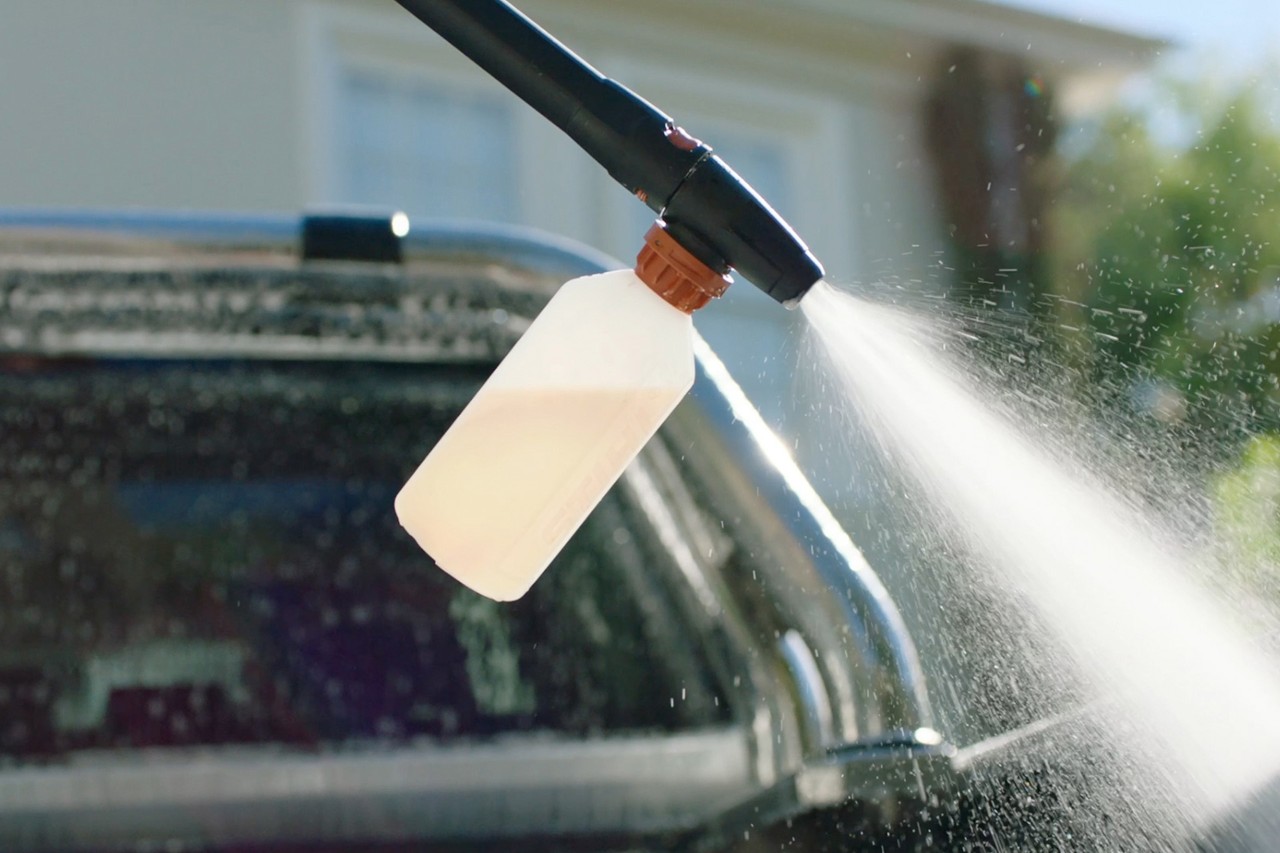 A STIHL RE 130 pressure washer with foam nozzle attached, applying car shampoo to a car