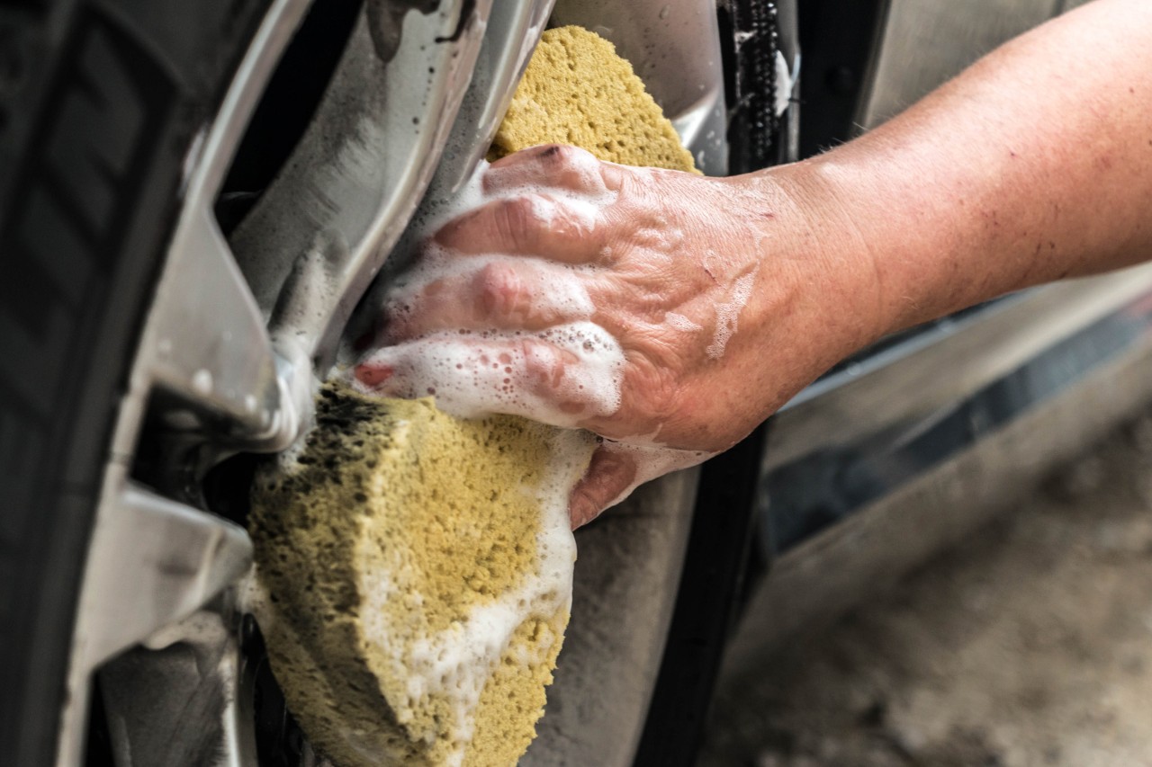 Close-up of car wheel rims being cleaned with a sponge
