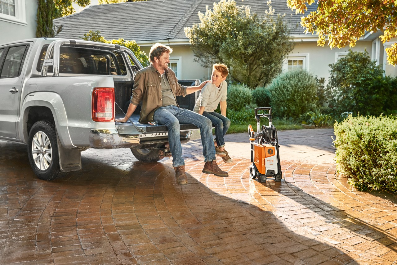 A man and young boy sitting on the truck bed of a pick-up, with a STIHL RE 130 plus pressure washer beside the vehicle