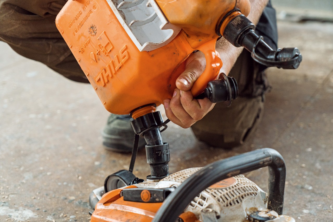 Close-up of a chainsaw being filled from a combination canister