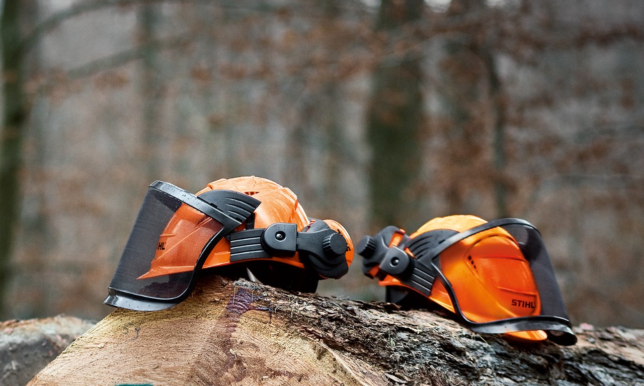 Two STIHL ADVANCE helmet sets resting on felled tree trunks in a forest