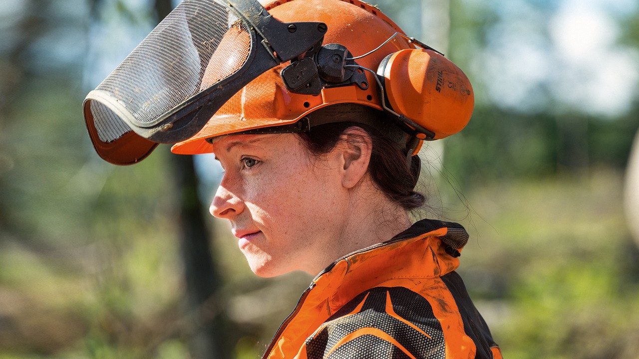 A woman wearing a STIHL helmet set including face protection, ear protection and helmet