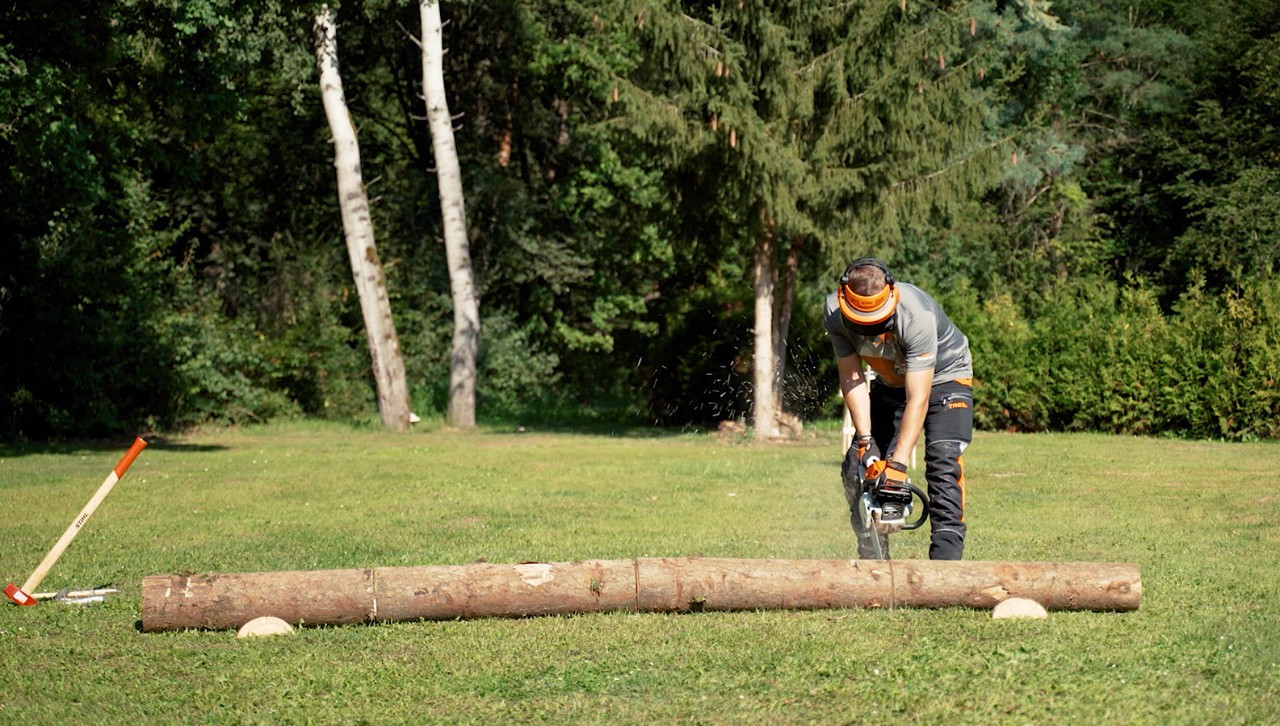 A person wearing protective gear uses a STIHL chainsaw to cut a tree trunk into firewood