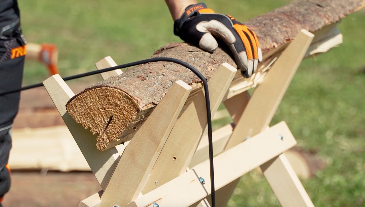 To cut firewood, a log is secured on a sawhorse using a lashing strap