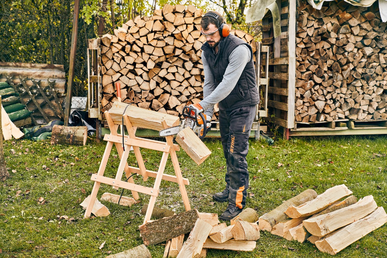 A metre-long piece of wood on a sawhorse being cut into firewood with the STIHL MS 180 petrol-driven chainsaw