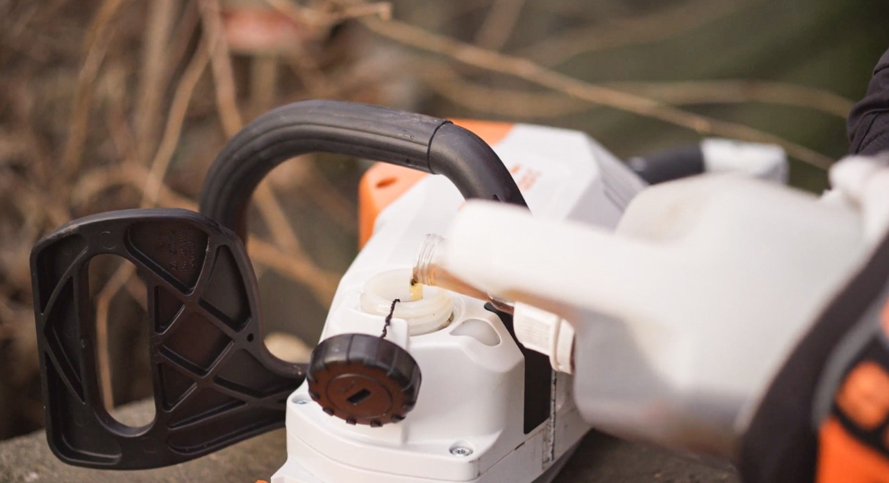 A STIHL MSA 120 cordless chainsaw being filled with chain oil