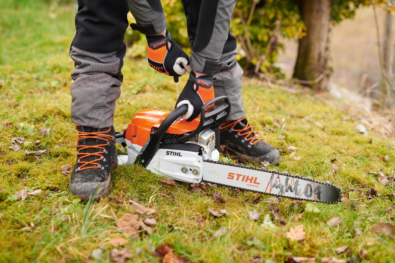 Someone wearing gloves performs a ground start of a STIHL MS 261 C-M petrol chainsaw with Light 04 guide bar