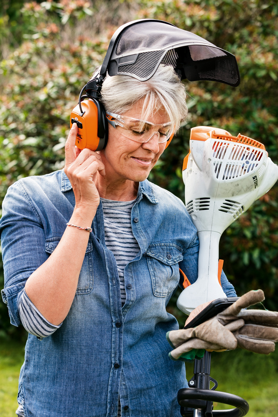 A woman wearing STIHL DYNAMIC BT-N combined ear and face protection, holding a STIHL FS 58 R petrol grass trimmer