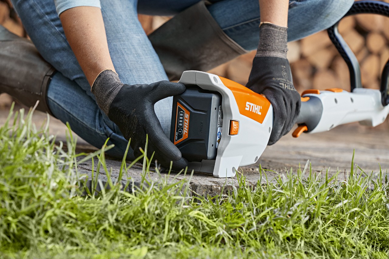 A person kneeling on the floor removing a battery from a STIHL FSA 57 cordless brushcutter