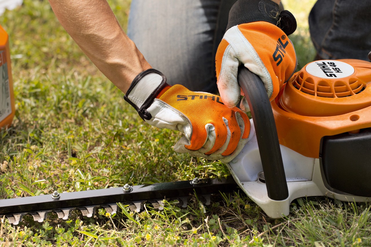 Close-up of a STIHL HS 46 petrol hedge trimmer being wiped with a cloth