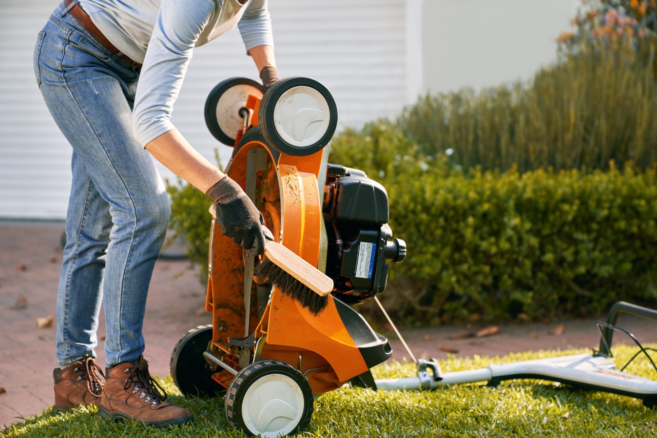 An upturned STIHL RM 448 T-C petrol lawn mower being cleaned with a hand brush