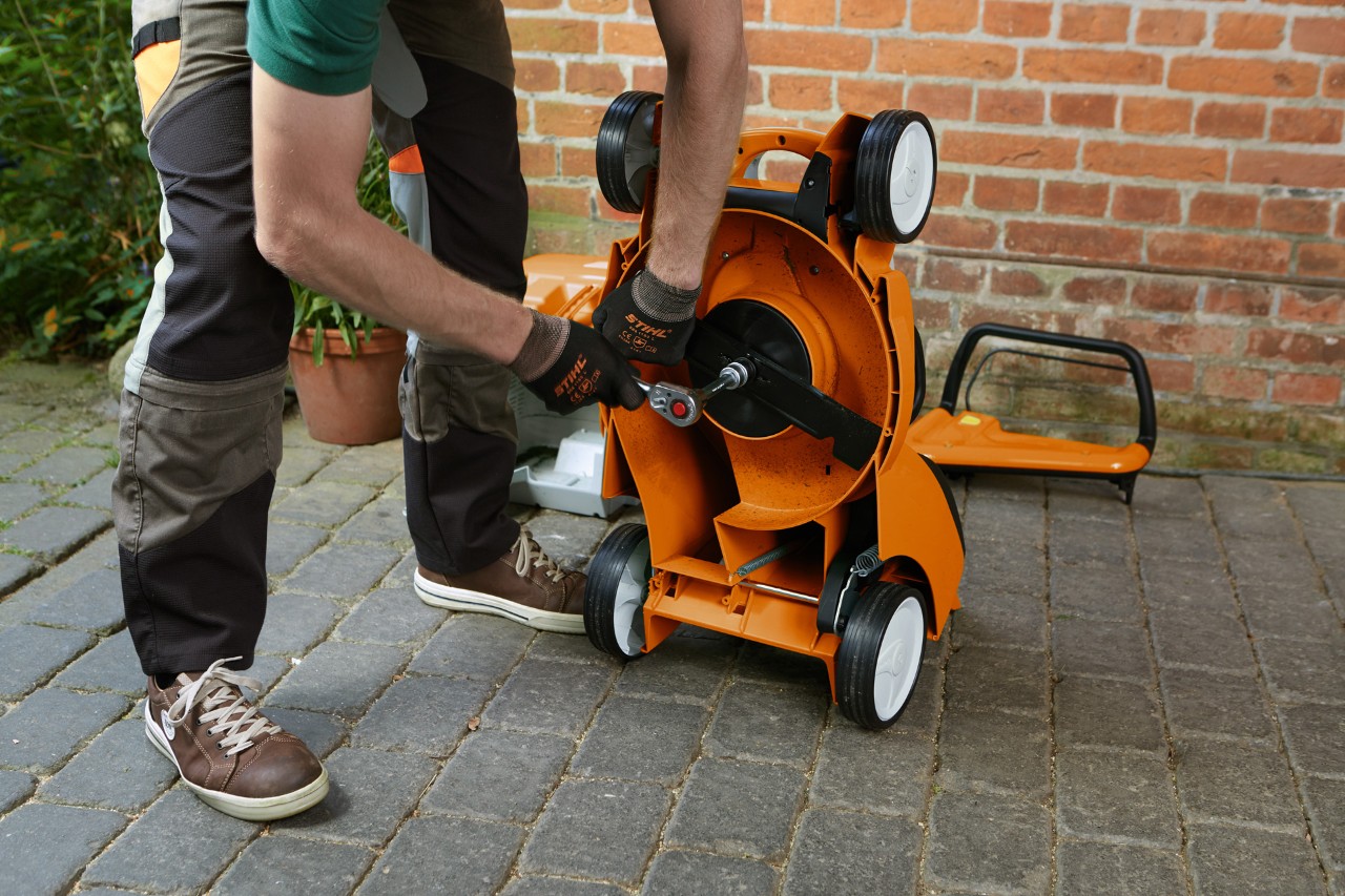 A person wearing gloves removing the blade from a tipped-up STIHL RM lawn mower