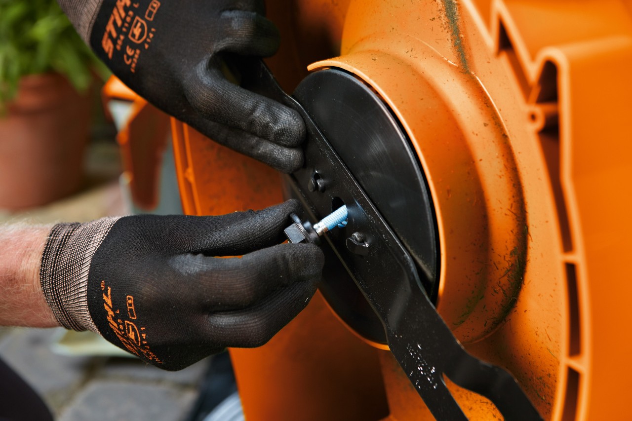 Close-up of the bolt being removed from a lawn mower blade by someone wearing gloves