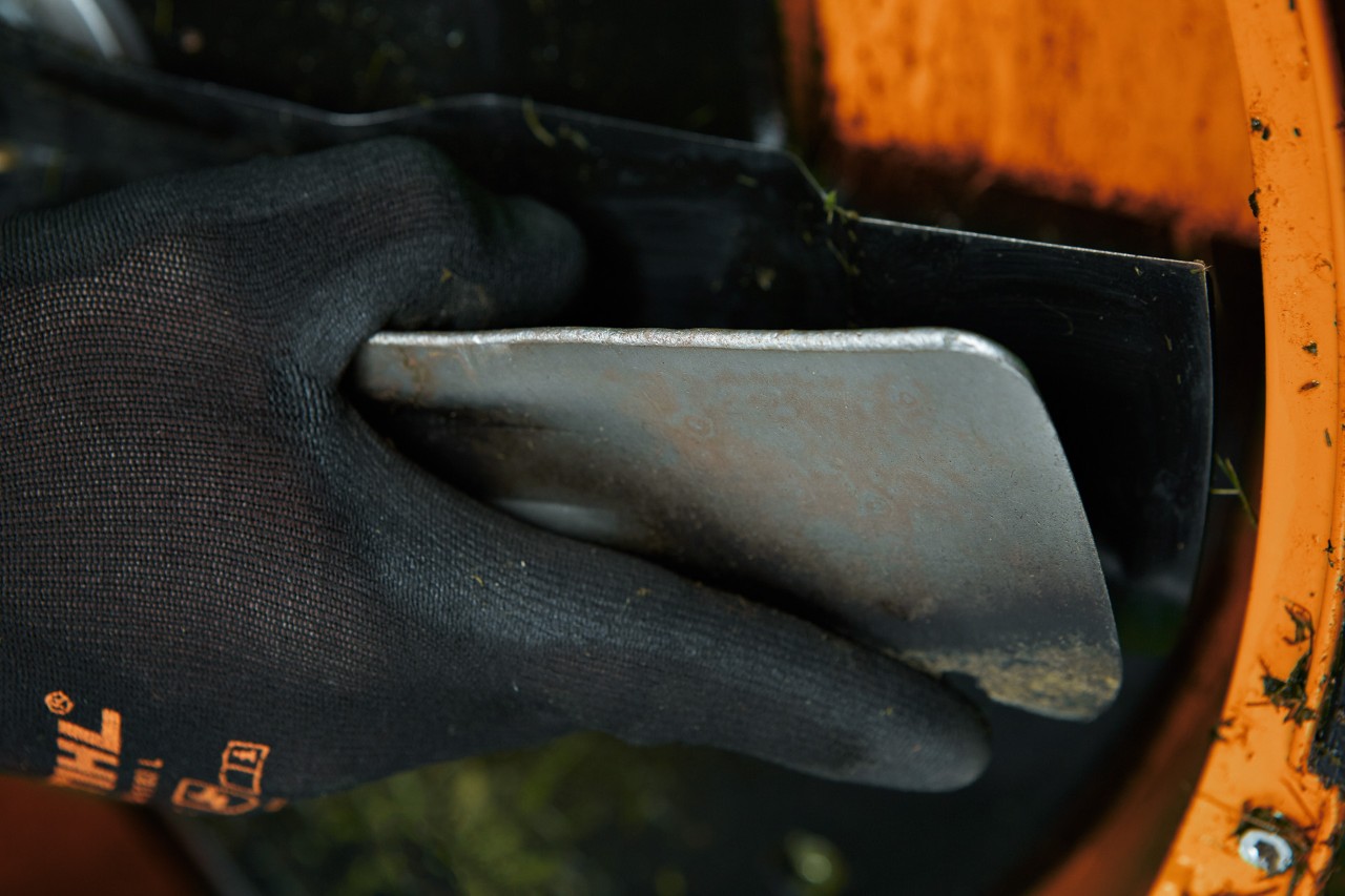 Close-up of a spatula being used to clean the underside of a lawn mower