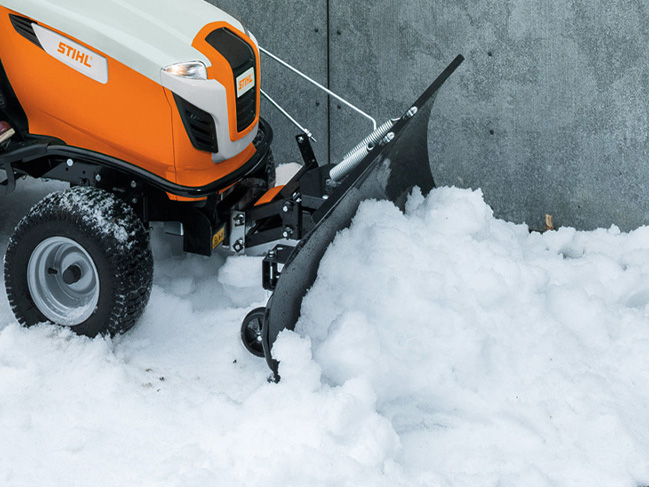 Snow is cleared from a wall with a snow blade on a lawn tractor