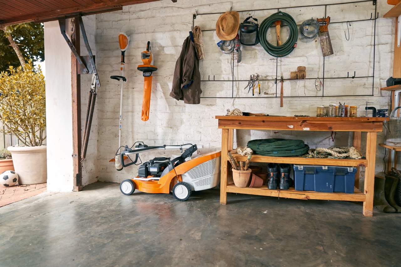 A STIHL RMA 339 C cordless lawn mower safely stored in a tidy garage with a workbench and hanging tools