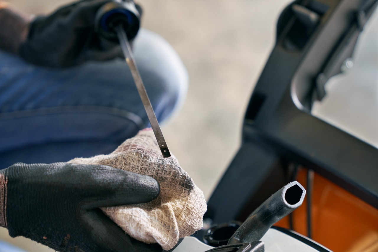 Close-up of a lawn mower dipstick that is being held over a rag to check the oil level