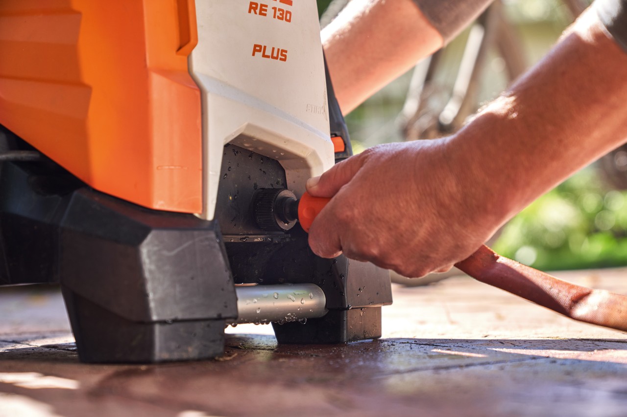 A person connecting a garden hose to the STIHL RE 130 PLUS high-pressure cleaner to use it