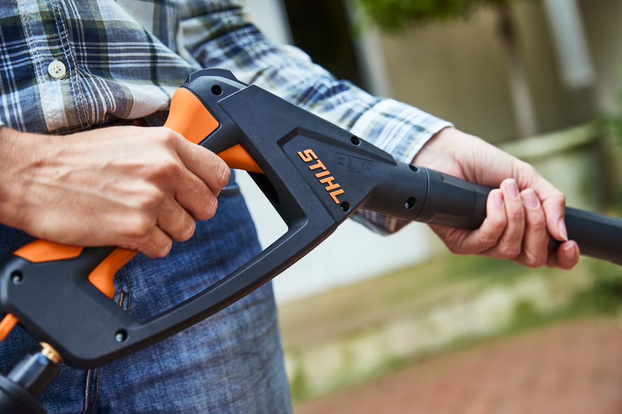 A person uses a STIHL RE 130 PLUS high-pressure cleaner by holding the trigger of the spray gun