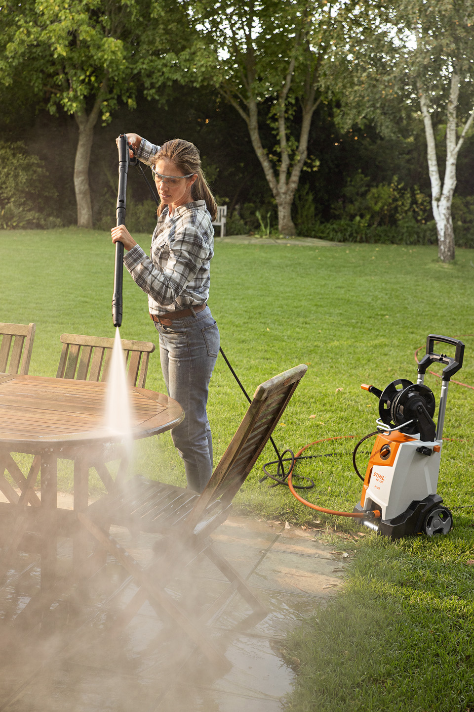 A woman using the STIHL RE 130 PLUS high-pressure cleaner outside to clean garden furniture