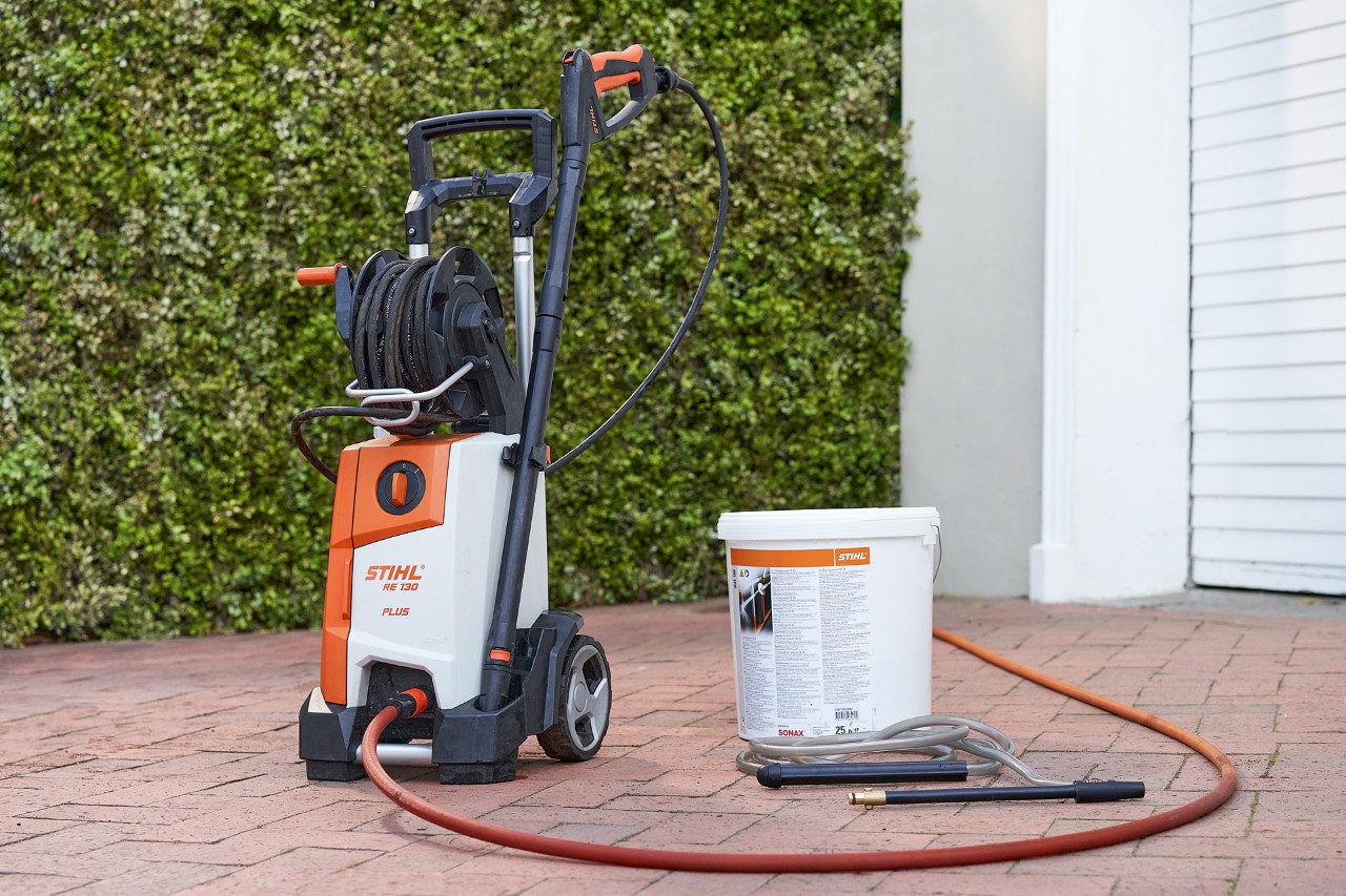STIHL RE 130 PLUS high-pressure cleaner and SB 90 blasting granulate for wet blasting in front of a garage 