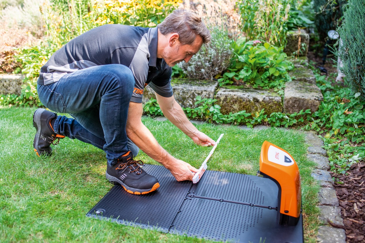 A STIHL dealer fitting the docking station for a STIHL iMOW® 422 robot mower in a  garden