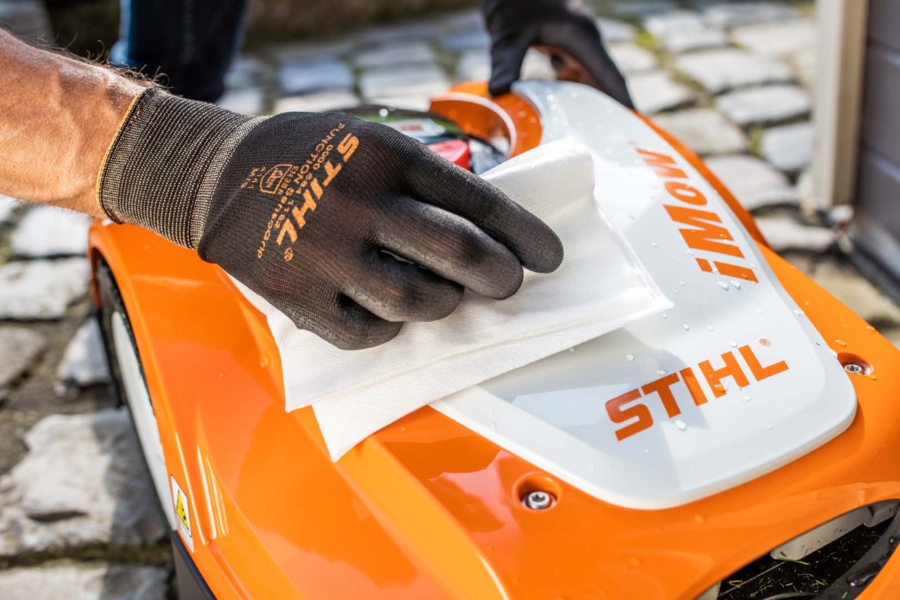 Close-up of the top of a STIHL iMOW® robot mower as someone wearing gloves wipes it with a cloth