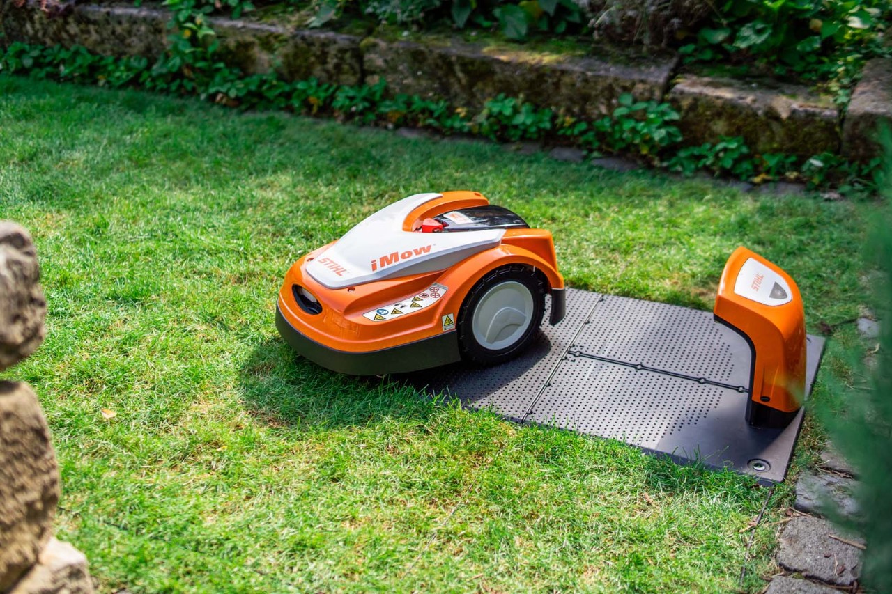 A STIHL iMOW® robot mower beside its docking station on a green lawn