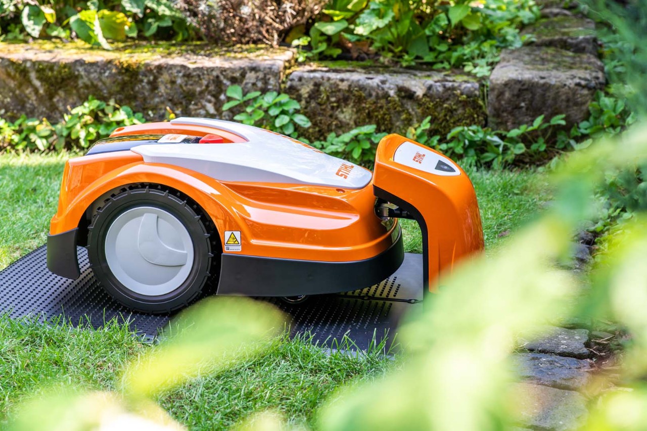 A STIHL iMOW® 422 robot lawn mower in a garden, recharging in its docking station