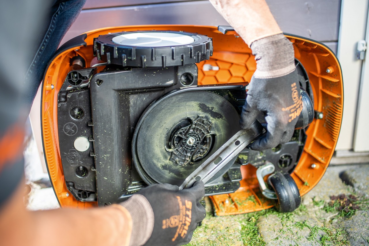 The cutting blade being removed from a STIHL iMOW® 422 robot lawn mower by a person wearing gloves