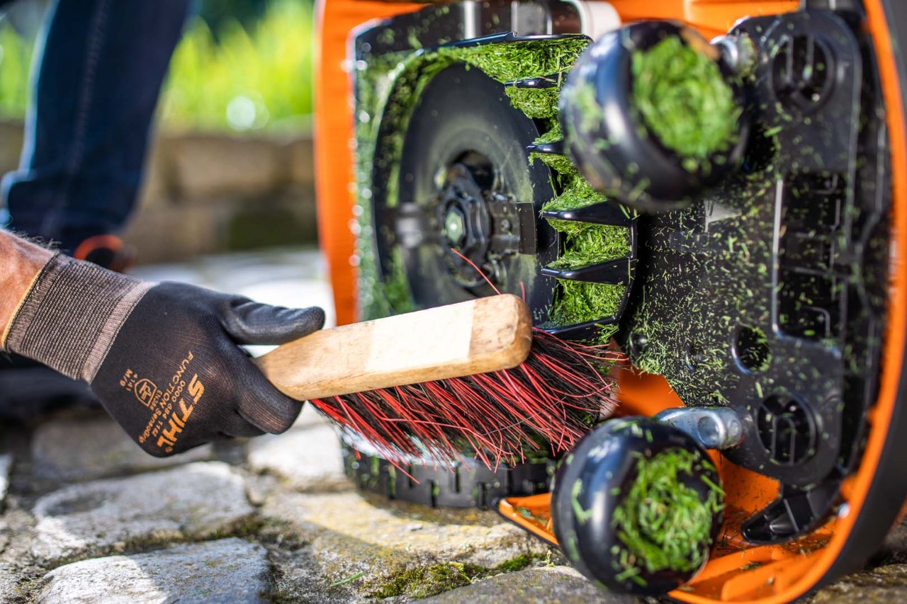 The underside of a STIHL iMOW® 422 robot lawn mower being cleaned with a brush