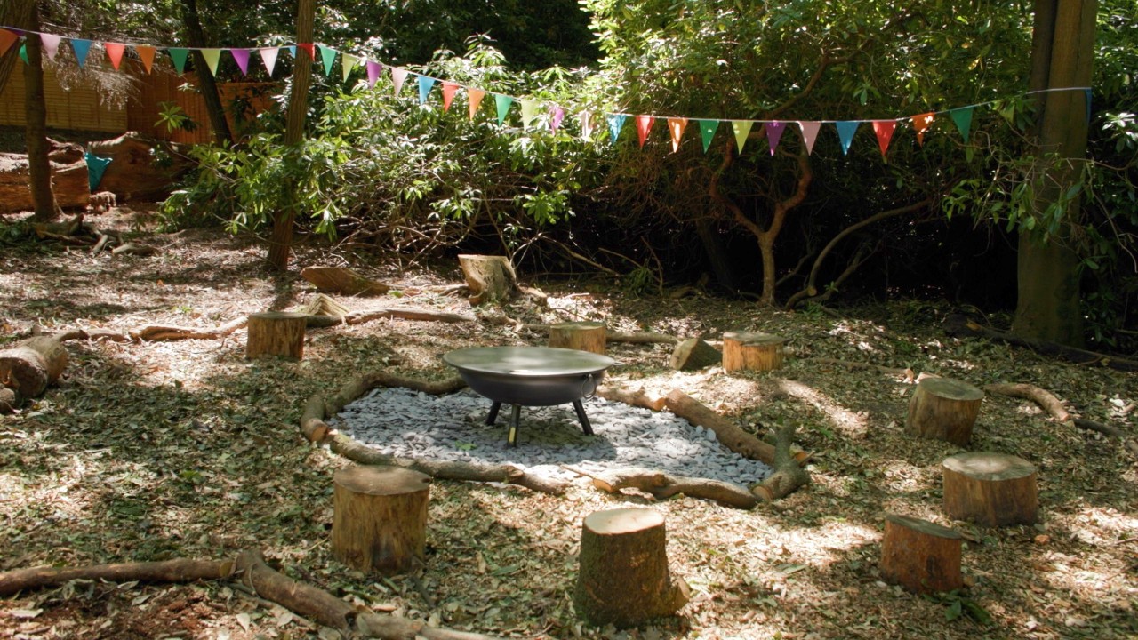 firepit with seating and colourful bunting strung between trees surrounding a seated area
