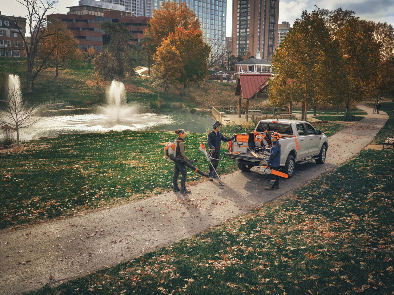 A group of professional landscapers stands around their vehicles, getting ready for work with STIHL cordless tools.
